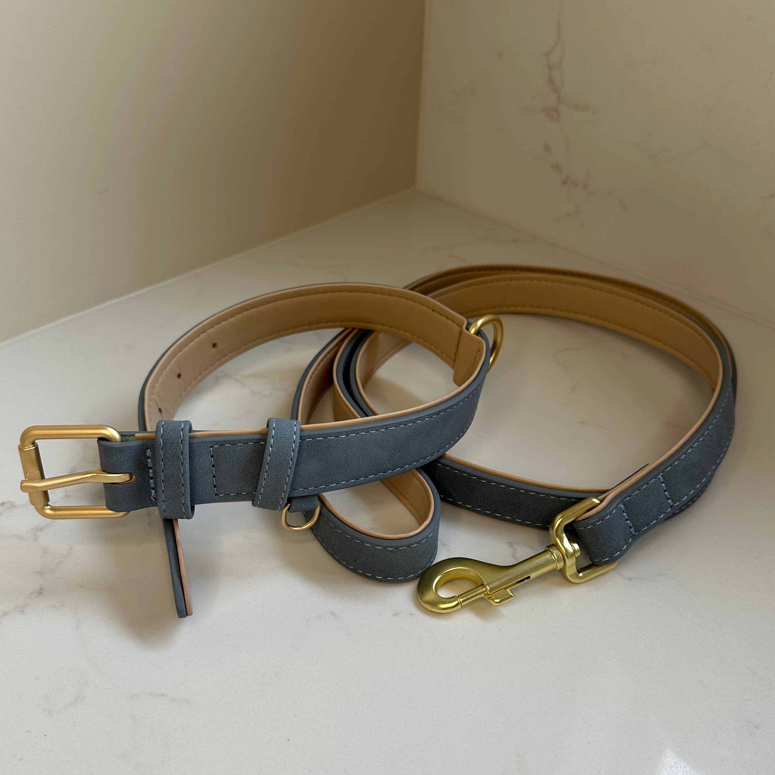 Two leather dog collars with brass hardware on a textured white surface
